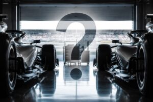 Two Mercedes Formula 1 cars in a garage with a question mark between them