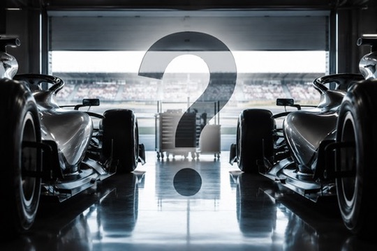 Two Mercedes Formula 1 cars in a garage with a question mark between them